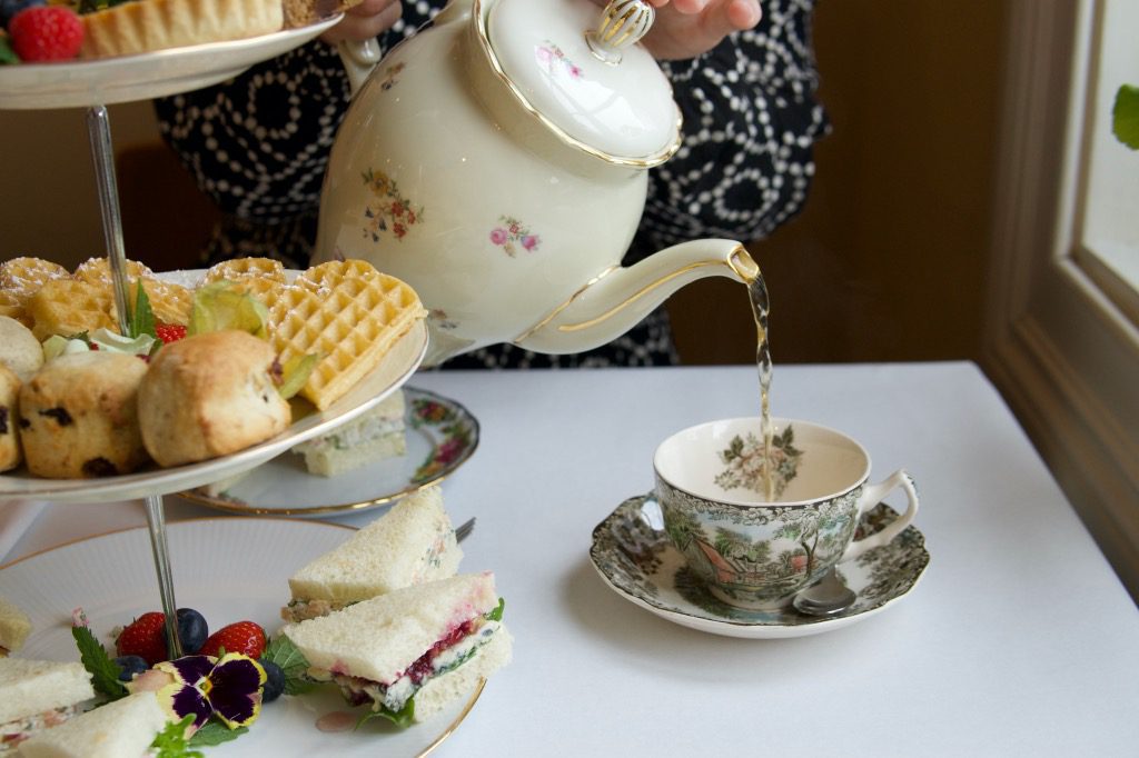 Afternoon tea på Jæren, te helles i kopp fra en stor kanne med et etasjefat på siden. Foto.